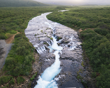 Aerial view of Bruara river with its turquoise water flowing through dark volcanic rocks and lush green shrubs Bruarfoss waterfall Iceland Aerial view of Bruara river with its turquoise water flowing through dark volcanic rocks and lush green shrubs Bruarfoss waterfall Iceland