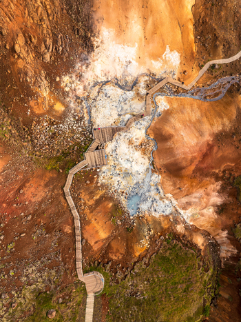 Aerial view of a wooden boardwalk winding through the vibrant mineral rich geothermal landscape of Iceland featuring steaming vents and colorful volcanic soil. Aerial view of a wooden boardwalk winding through the vibrant mineral rich geothermal landscape of Iceland featuring steaming vents and colorful volcanic soil.