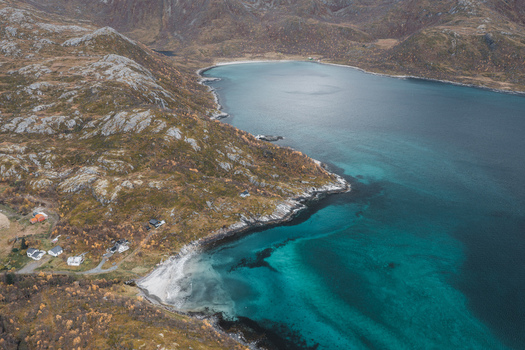 Aerial view of the rugged coastline of Senja featuring turquoise waters rocky cliffs and small houses nestled along the shore in Senja Troms Norway.