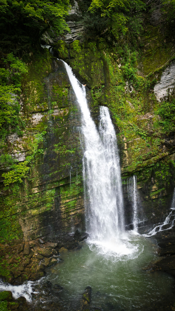 Aerial view of Cascades du Flumen waterfall cascading down a mossy rock face into a pool surrounded by lush green forest in Septmoncel Les Molunes Bourgogne Franche Comte France. Aerial view of Cascades du Flumen waterfall cascading down a mossy rock face into a pool surrounded by lush green forest in Septmoncel Les Molunes Bourgogne Franche Comte France.