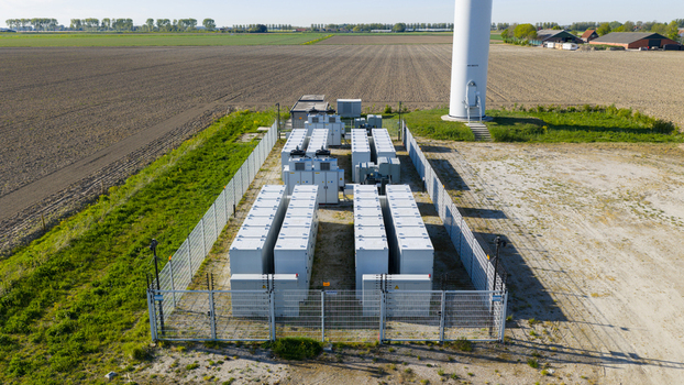 Aerial view of a battery energy storage system with rows of white units next to a wind turbine in a rural landscape under a clear sky in Ooltgensplaat Zuid Holland Netherlands. Aerial view of a battery energy storage system with rows of white units next to a wind turbine in a rural landscape under a clear sky in Ooltgensplaat Zuid Holland Netherlands.
