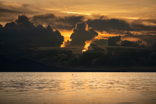 View of the tranquil ocean reflecting the golden light piercing through dark brooding clouds at sunset creating a dramatic contrast Gizo Solomon Islands. View of the tranquil ocean reflecting the golden light piercing through dark brooding clouds at sunset creating a dramatic contrast Gizo Solomon Islands.