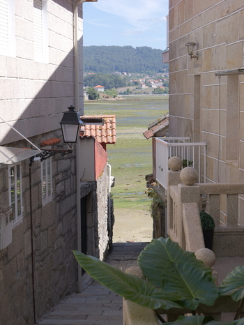 View of a narrow stone alleyway in the historic village of Combarro leading towards the tidal flats and distant hills with traditional stone architecture and a lantern in Combarro Pontevedra Spain.
