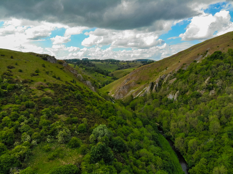 Aerial view of the lush green Manifold Valley with limestone cliffs winding river and dramatic clouds over the rolling hills of the Peak District in Wetton England United Kingdom. Aerial view of the lush green Manifold Valley with limestone cliffs winding river and dramatic clouds over the rolling hills of the Peak District in Wetton England United Kingdom.