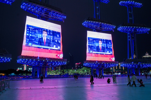 Guangzhou Guangdong Province China 24 February 2024 View of large LED screens displaying a news broadcast in a public square at night with people walking under blue lighting. Guangzhou Guangdong Province China 24 February 2024 View of large LED screens displaying a news broadcast in a public square at night with people walking under blue lighting.