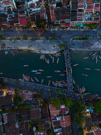 Aerial view of the Thu Bon River in Hoi An with traditional wooden boats a pedestrian bridge and historic yellow walled buildings in the old town of Vietnam. Aerial view of the Thu Bon River in Hoi An with traditional wooden boats a pedestrian bridge and historic yellow walled buildings in the old town of Vietnam.