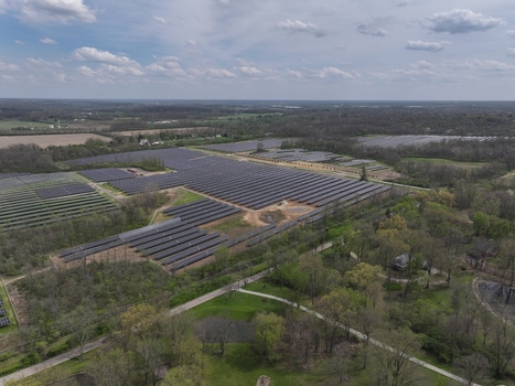 Lebanon United States 12 April 2026 Aerial view of a large solar farm with rows of photovoltaic panels surrounded by lush green trees and rural landscapes under a cloudy sky.