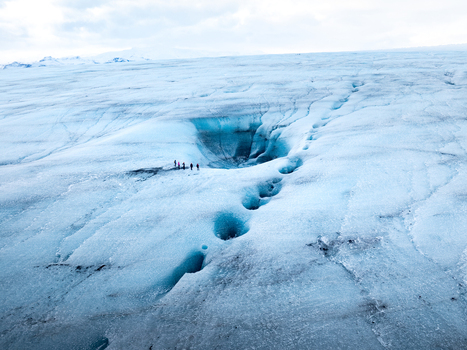 Aerial view of Breidamerkurjokull glacier with deep blue ice crevasses and a group of people standing near a large meltwater hole in Sveitarfelagid Hornafjordur Iceland. Aerial view of Breidamerkurjokull glacier with deep blue ice crevasses and a group of people standing near a large meltwater hole in Sveitarfelagid Hornafjordur Iceland.