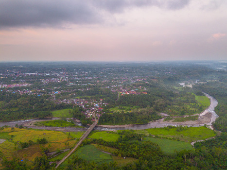 Aerial view of Taba Tembilang with a river flowing through lush green rice fields and a small village in Arga Makmur Bengkulu Indonesia.