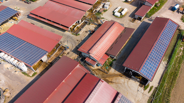Aerial view of a dairy farm featuring multiple buildings with red roofs and solar panels silos and surrounding agricultural land in San Giuliano Milanese Lombardy Italy.