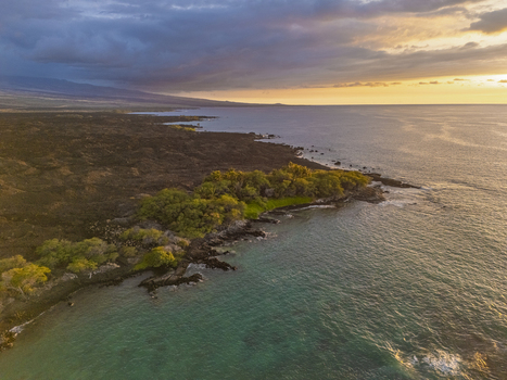 Aerial view of Waikoloa Beach with dark volcanic lava fields meeting the turquoise ocean under a dramatic sunset sky Waikoloa Village Hawaii United States.