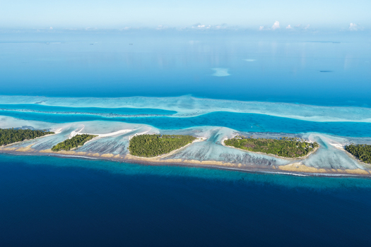 Aerial view of lush tropical islands with green palm trees and turquoise coral reefs surrounded by the deep blue ocean under a clear sky near Vaanee Dhaalu Atoll Maldives. Aerial view of lush tropical islands with green palm trees and turquoise coral reefs surrounded by the deep blue ocean under a clear sky near Vaanee Dhaalu Atoll Maldives.