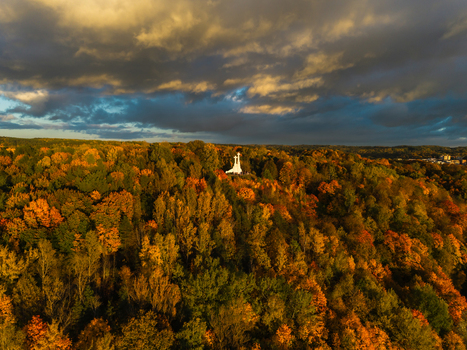 Aerial view of the Three Crosses monument standing tall amidst a sea of autumnal foliage painted in fiery golds and rustic oranges under a dramatic sky Vilnius Lithuania. Aerial view of the Three Crosses monument standing tall amidst a sea of autumnal foliage painted in fiery golds and rustic oranges under a dramatic sky Vilnius Lithuania.