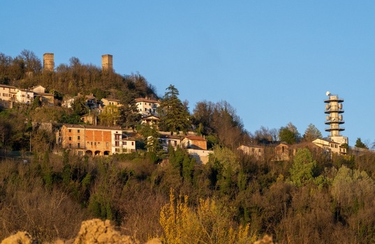 Aerial view of the Television Tower Tortona and historic stone towers on a wooded hillside with residential houses Tortona Piedmont Italy.
