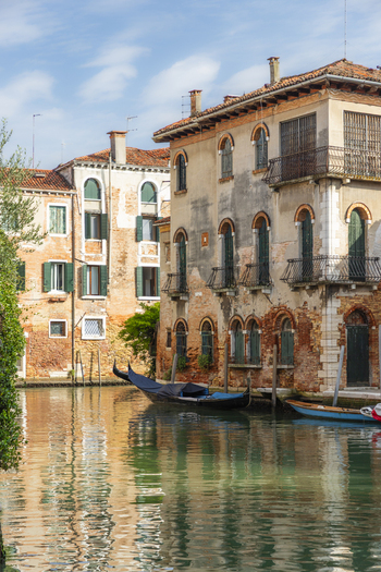 View of a traditional gondola moored in a quiet canal lined with historic weathered brick buildings and green shutters in Venice Veneto Italy. View of a traditional gondola moored in a quiet canal lined with historic weathered brick buildings and green shutters in Venice Veneto Italy.