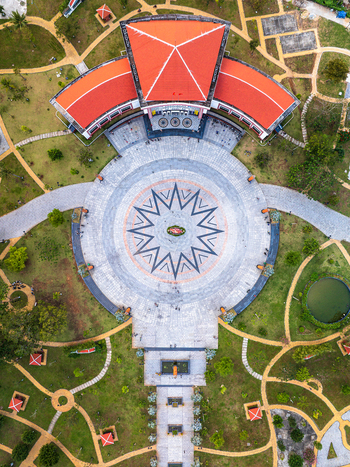 Aerial view of a building with a red roof and a large circular plaza featuring a star pattern surrounded by a park with pathways and a small pond in Vietnam. Aerial view of a building with a red roof and a large circular plaza featuring a star pattern surrounded by a park with pathways and a small pond in Vietnam.
