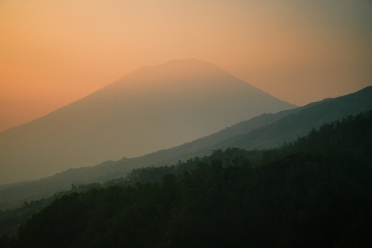 View of Mount Batur at sunrise with hazy atmosphere and forested slopes in Kintamani Bali Indonesia.