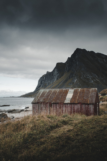 View of Vikten Beach featuring a weathered red wooden shed by the rocky coastline under a dramatic cloudy sky in Vikten Nordland Norway.