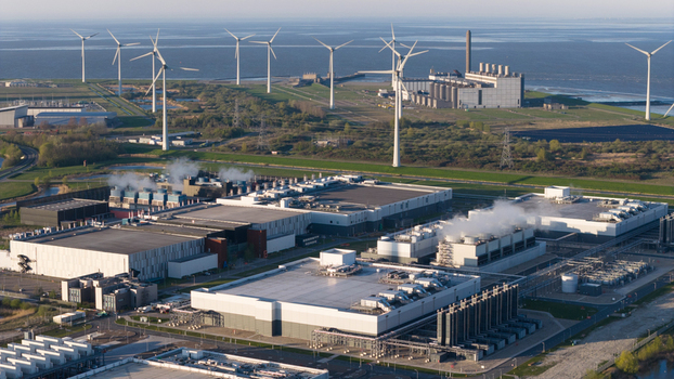 Aerial view of the industrial port area featuring a large data center complex with steam rising wind turbines and a power plant along the coast in Eemshaven Groningen Netherlands. Aerial view of the industrial port area featuring a large data center complex with steam rising wind turbines and a power plant along the coast in Eemshaven Groningen Netherlands.