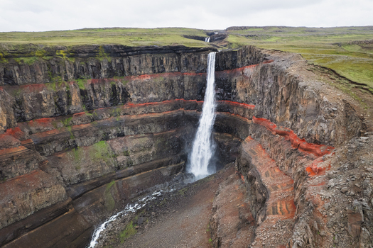Aerial view of Hengifoss waterfall cascading down basaltic cliffs with visible red clay layers in Egilsstadir Fljotsdalshreppur Iceland. Aerial view of Hengifoss waterfall cascading down basaltic cliffs with visible red clay layers in Egilsstadir Fljotsdalshreppur Iceland.