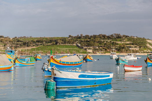 View of vibrant colorful traditional fishing boats bobbing gently on the tranquil azure waters reflecting the clear sky Marsaxlokk Malta. View of vibrant colorful traditional fishing boats bobbing gently on the tranquil azure waters reflecting the clear sky Marsaxlokk Malta.