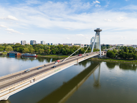 Aerial view of Most SNP bridge with its iconic UFO observation deck over the Danube river surrounded by lush green trees and city buildings Bratislava Bratislava Region Slovakia. Aerial view of Most SNP bridge with its iconic UFO observation deck over the Danube river surrounded by lush green trees and city buildings Bratislava Bratislava Region Slovakia.