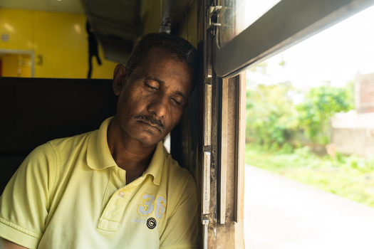 Sri Lanka 06 February 2026 View of a man sleeping with his head resting against a window inside a train carriage as it passes through a rural landscape.