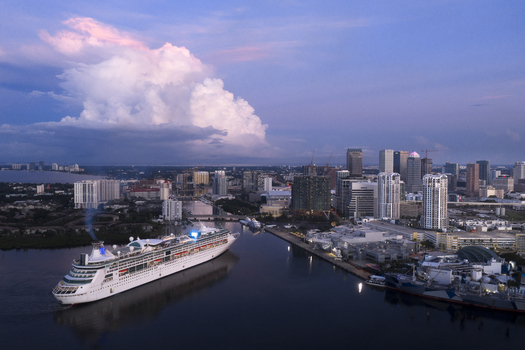 Tampa United States 04 July 2026 Aerial view of Tampa Cruise Terminal 6 with a large cruise ship departing surrounded by the city skyline calm harbor waters and dramatic clouds at sunset.