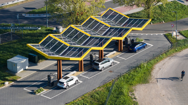 Bant Netherlands 23 April 2026 Aerial view of Fastned charging station with its iconic yellow solar roof electric cars parked at charging points and a cyclist on the road. Bant Netherlands 23 April 2026 Aerial view of Fastned charging station with its iconic yellow solar roof electric cars parked at charging points and a cyclist on the road.