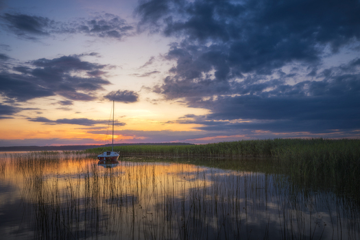 View of Lake Lasmiady with a sailboat moored among reeds at sunset under a dramatic cloudy sky in Elk Warminsko Mazurskie Poland.