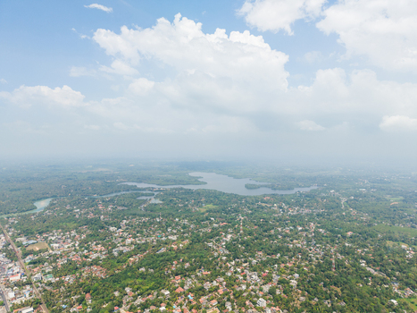 Aerial view of dense tropical vegetation and residential houses with red roofs near a distant lake under a cloudy sky in Hikkaduwa Southern Province Sri Lanka. Aerial view of dense tropical vegetation and residential houses with red roofs near a distant lake under a cloudy sky in Hikkaduwa Southern Province Sri Lanka.