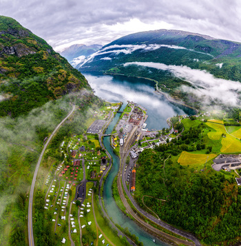 Aerial view of the village of Flam nestled in the Aurlandsfjord valley featuring the railway station lush green mountains winding river and misty clouds in Flam Vestland Norway. Aerial view of the village of Flam nestled in the Aurlandsfjord valley featuring the railway station lush green mountains winding river and misty clouds in Flam Vestland Norway.