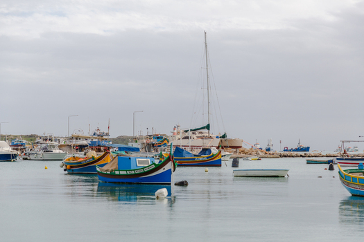 View of vibrant colorful traditional fishing boats bobbing gently on the calm reflective waters of the harbor Marsaxlokk Malta. View of vibrant colorful traditional fishing boats bobbing gently on the calm reflective waters of the harbor Marsaxlokk Malta.