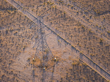 Aerial view of a high voltage power line tower standing in a dry desert landscape with sparse vegetation and a dirt road Enterprise Nevada United States. Aerial view of a high voltage power line tower standing in a dry desert landscape with sparse vegetation and a dirt road Enterprise Nevada United States.