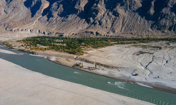 Aerial view of the Sarfaranga Cold Desert Shigar with its vast sandy dunes the flowing river and lush green vegetation set against the rugged mountain landscape in Skardu Gilgit Pakistan.