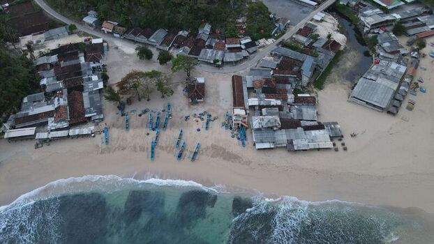 Aerial view of Pantai Drini featuring traditional fishing boats lined up on the sandy shore surrounded by coastal houses in Kecamatan Tanjungsari Daerah Istimewa Yogya Indonesia. Aerial view of Pantai Drini featuring traditional fishing boats lined up on the sandy shore surrounded by coastal houses in Kecamatan Tanjungsari Daerah Istimewa Yogya Indonesia.