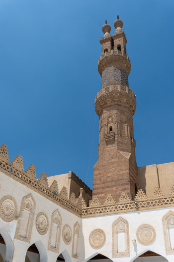 View of the Al Azhar Mosque minaret with intricate stone carvings and decorative courtyard walls under a clear blue sky Cairo Egypt. View of the Al Azhar Mosque minaret with intricate stone carvings and decorative courtyard walls under a clear blue sky Cairo Egypt.