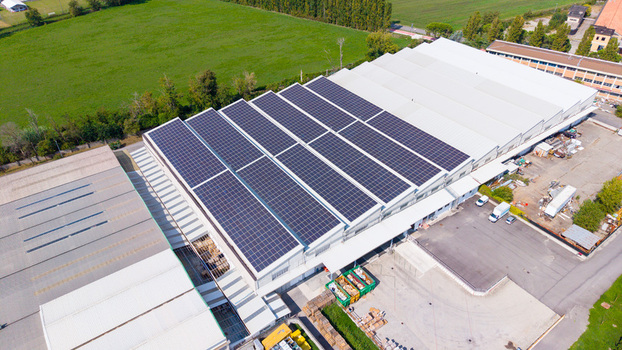 Aerial view of a distribution center featuring a large roof covered with solar panels surrounded by industrial grounds and green fields in Milan Lombardy Italy. Aerial view of a distribution center featuring a large roof covered with solar panels surrounded by industrial grounds and green fields in Milan Lombardy Italy.