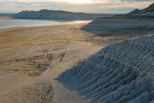 Aerial view of Tuzbair salt flats with white limestone cliffs textured desert terrain and tire tracks under soft golden hour light in Mangystau District Mangystau Region Kazakhstan.