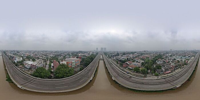 Aerial view of the elevated highway stretching over a river surrounded by dense urban residential areas and lush greenery under a cloudy sky in Bekasi Barat West Java Indonesia. Aerial view of the elevated highway stretching over a river surrounded by dense urban residential areas and lush greenery under a cloudy sky in Bekasi Barat West Java Indonesia.