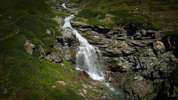 Aerial view of a cascade of water tumbling over the rugged dark rocks contrasting against the vibrant green slopes Valgrisenche Aosta Valley Italy.