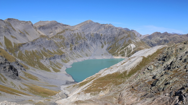 View of Lac du Vieux Emosson surrounded by rugged rocky mountain peaks and steep slopes under a clear blue sky in Finhaut Valais Switzerland. View of Lac du Vieux Emosson surrounded by rugged rocky mountain peaks and steep slopes under a clear blue sky in Finhaut Valais Switzerland.