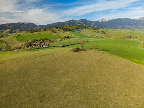 Aerial view of rolling green hills and a small village with the Tatra mountains in the background under a blue sky Liptovsky Trnovec Zilina Region Slovakia.