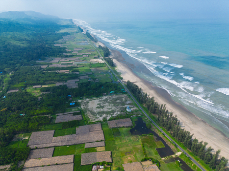 Aerial view of the long sandy coastline of Cox s Bazar beach with waves a coastal road and lush green vegetation in Cox s Bazar Chittagong Division Bangladesh. Aerial view of the long sandy coastline of Cox s Bazar beach with waves a coastal road and lush green vegetation in Cox s Bazar Chittagong Division Bangladesh.