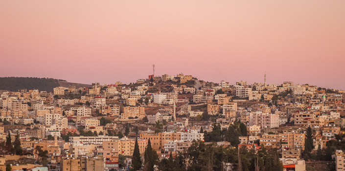 View of the cityscape of Jerash at sunset with residential buildings minarets and hilly terrain in Jerash Jerash Governorate Jordan. View of the cityscape of Jerash at sunset with residential buildings minarets and hilly terrain in Jerash Jerash Governorate Jordan.