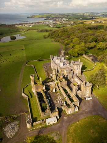 Aerial view of the historic ruins of Castlefreke Castle surrounded by lush green fields dense woodlands and the rugged coastline in Castlefreke County Cork Ireland.