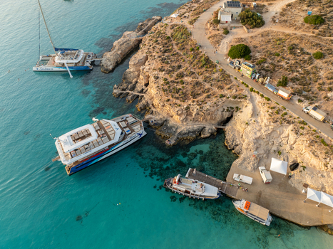 Aerial view of turquoise waters embrace the rugged coastline where boats and ferries dock contrasting with the arid landscape Blue lagoon Comino Malta. Aerial view of turquoise waters embrace the rugged coastline where boats and ferries dock contrasting with the arid landscape Blue lagoon Comino Malta.