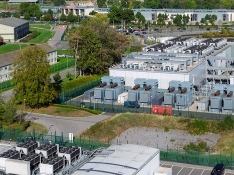 Aerial view of a data center facility with industrial cooling units fenced perimeter and surrounding parking area in the United Kingdom.