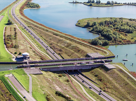 Aerial view of Naviduct Krabbersgat with boats navigating the lock system and a highway passing over the water surrounded by green embankments in Lelystad Flevoland Netherlands. Aerial view of Naviduct Krabbersgat with boats navigating the lock system and a highway passing over the water surrounded by green embankments in Lelystad Flevoland Netherlands.