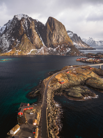 Aerial view of a winding road connecting islands under the gaze of snow dusted peaks reflecting in the dark waters Sakris&oslash;ya Norway.